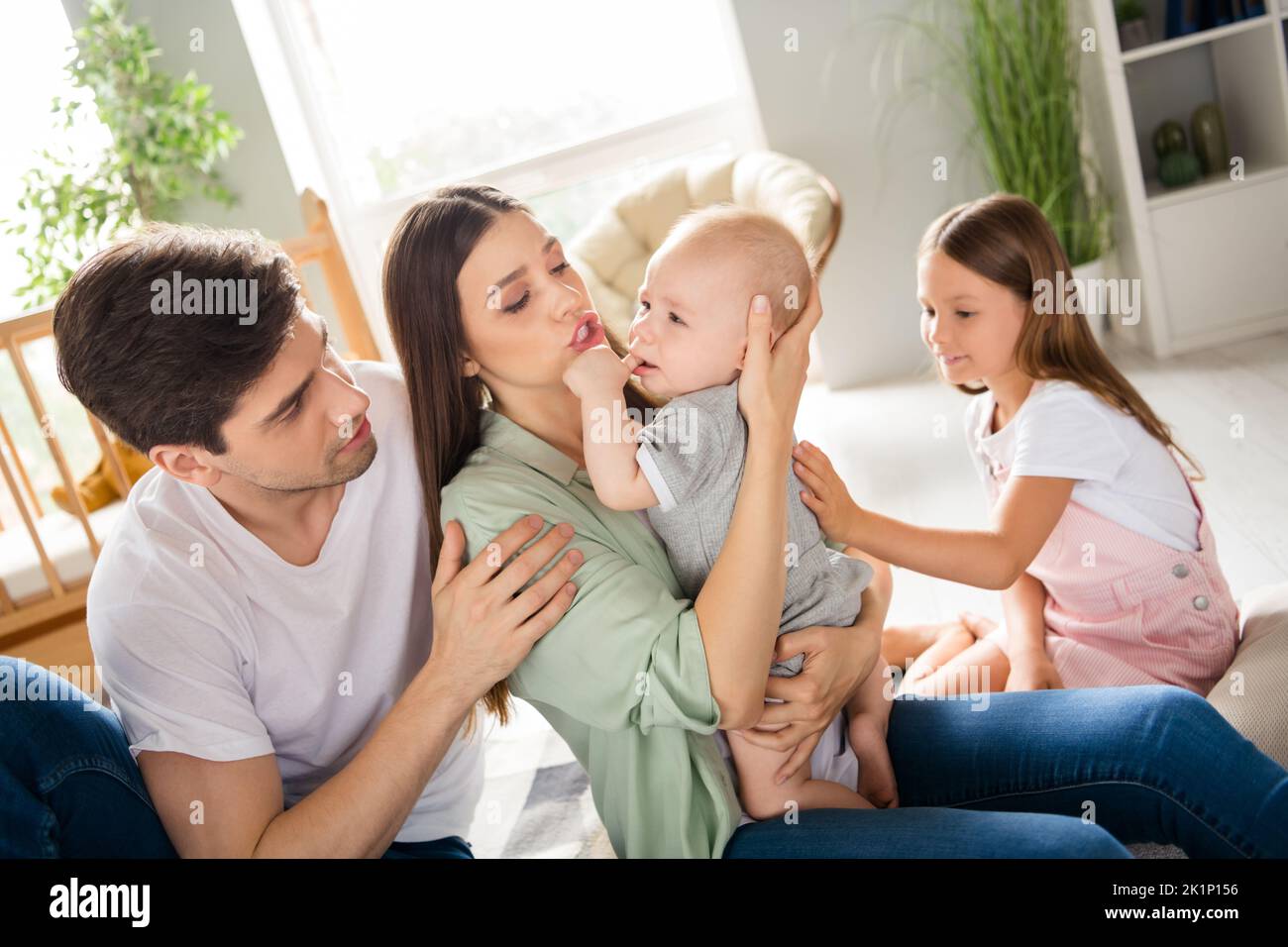 Photo de doux couple mignon deux enfants assis tapis apaisant petit bébé à l'intérieur maison maison chambre Banque D'Images