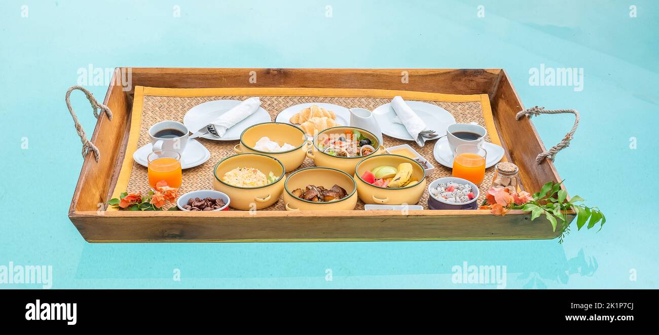 Plateau de petit-déjeuner flottant dans la piscine de l'hôtel de luxe ou de la villa tropicale, fruits, croissant, café et jus d'orange. Été exotique, détente Banque D'Images