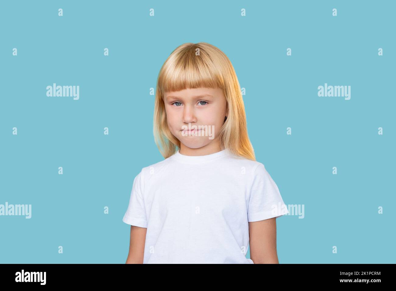 Gamin sarcastique. Petite enfance. Beauté innocente. Portrait de timide confondu mignon blond petite fille en blanc t-shirt regardant l'appareil photo isolé sur blu Banque D'Images