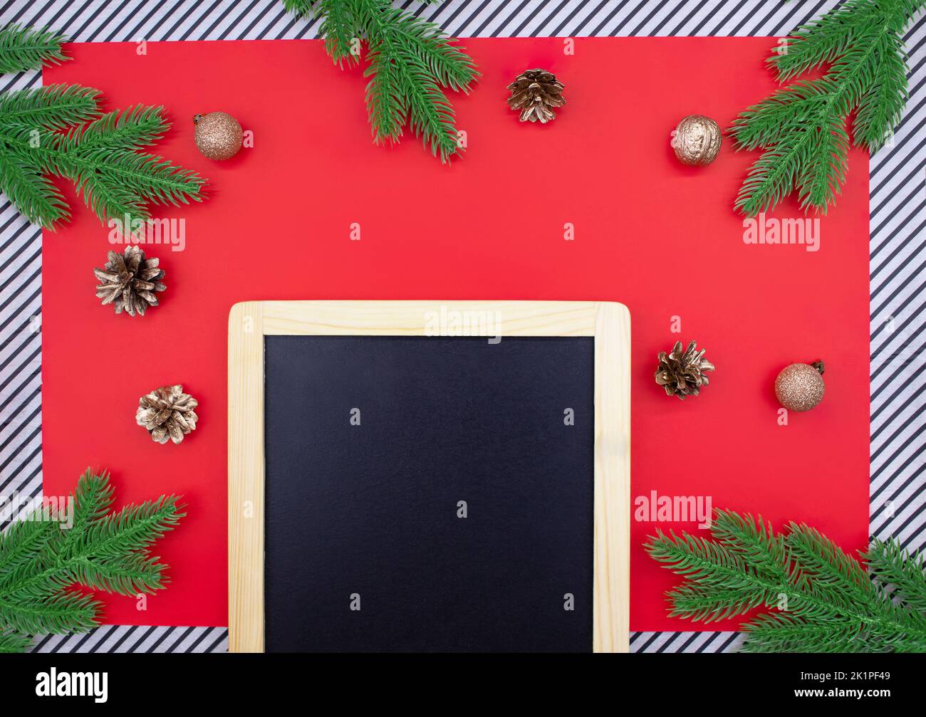 Tableau noir à craie pour annonce avec branches d'épinette, cônes dorés et noix, boules à paillettes sur fond rouge et rayures. Noël, nouvel an Banque D'Images