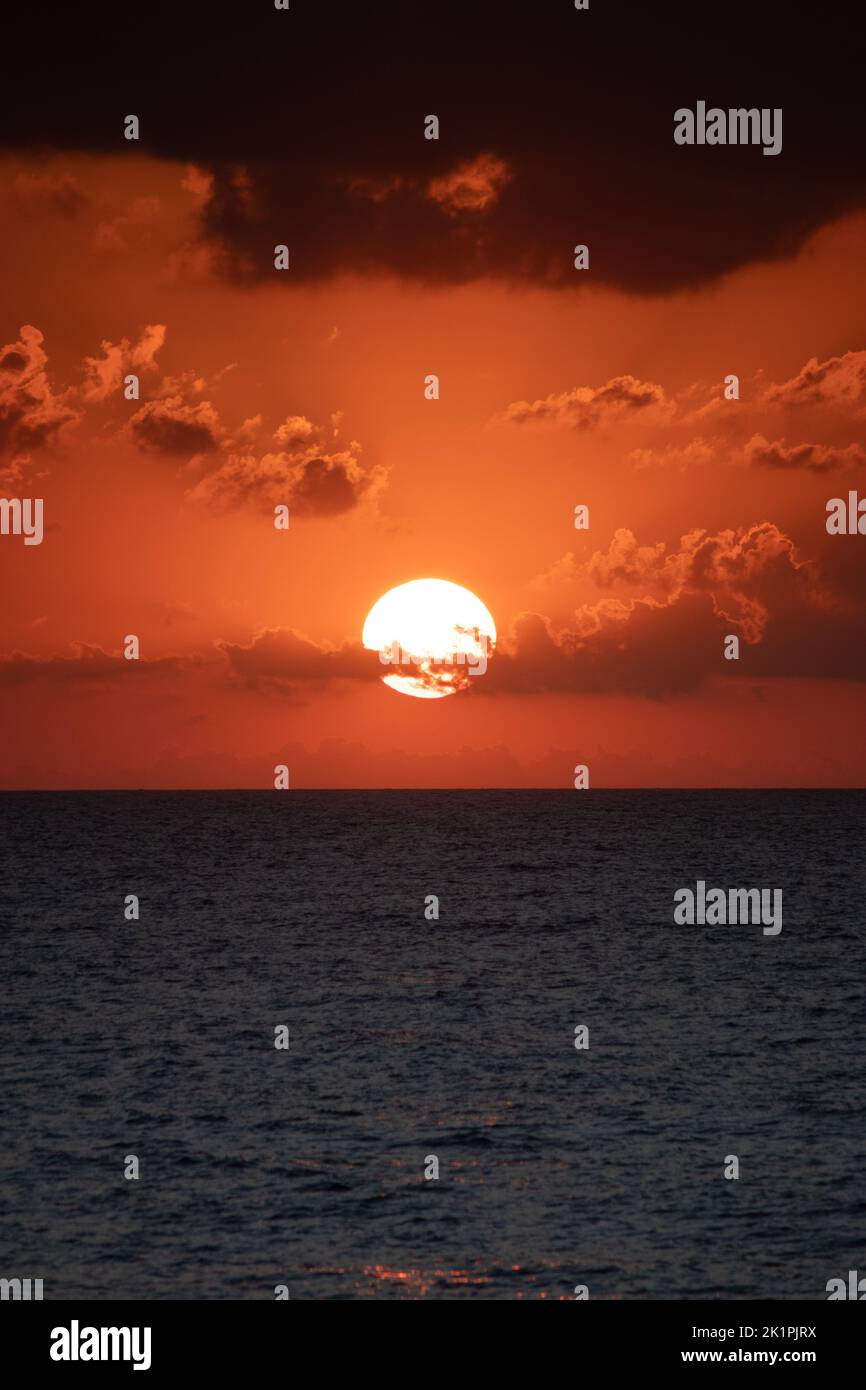 Photo de coucher de soleil verticale. La ligne séparant la mer et le ciel. Disque de soleil jaune vif derrière les nuages. Transition du jour à la nuit. Banque D'Images