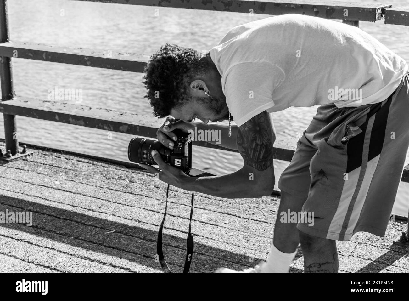 Échelle de gris d'un photographe afro-américain qui se penche vers le bas et prend des photos avec l'appareil photo Banque D'Images