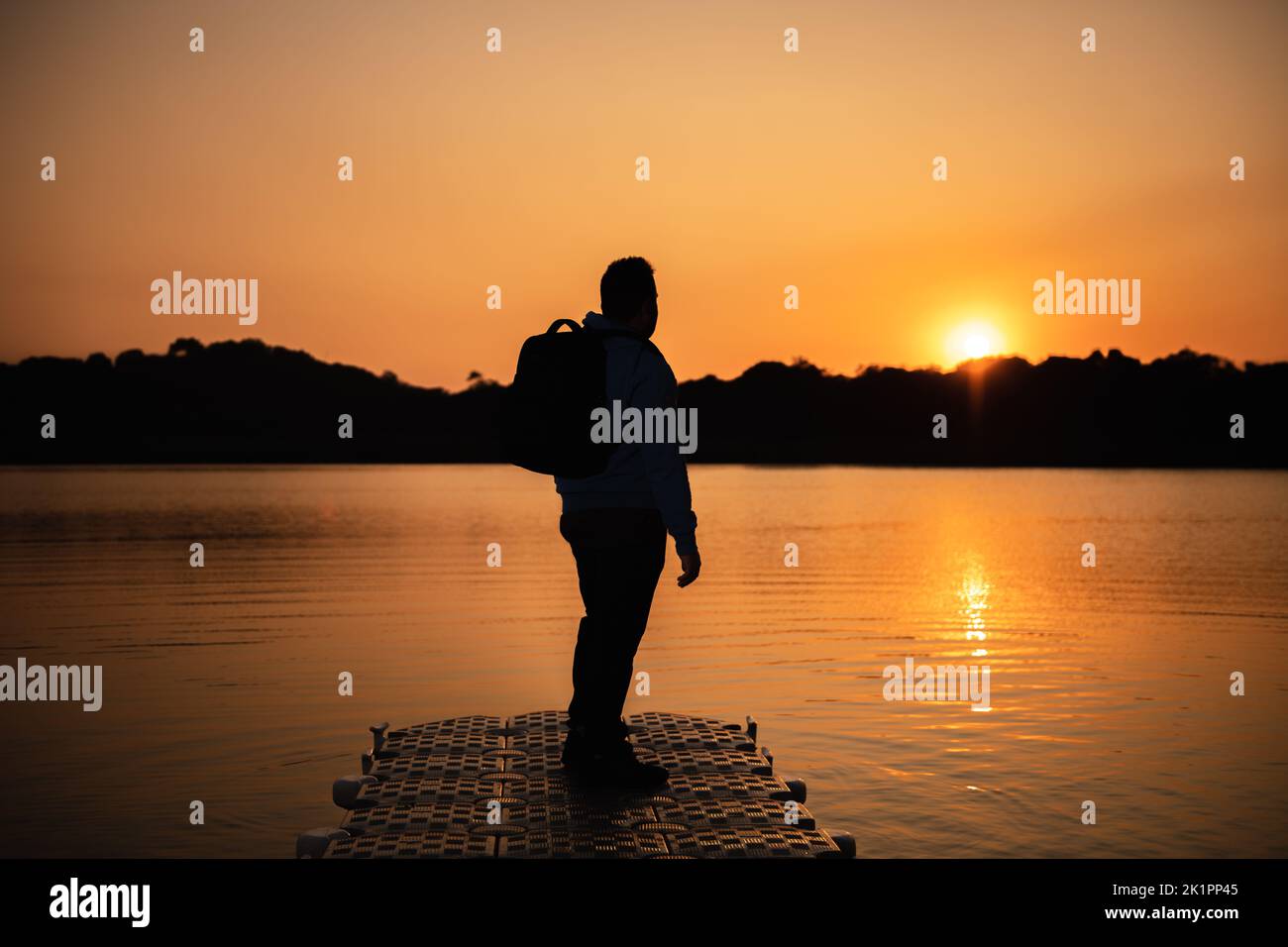 Une silhouette d'une personne avec un sac à dos sur une jetée dans le lac au coucher du soleil Banque D'Images