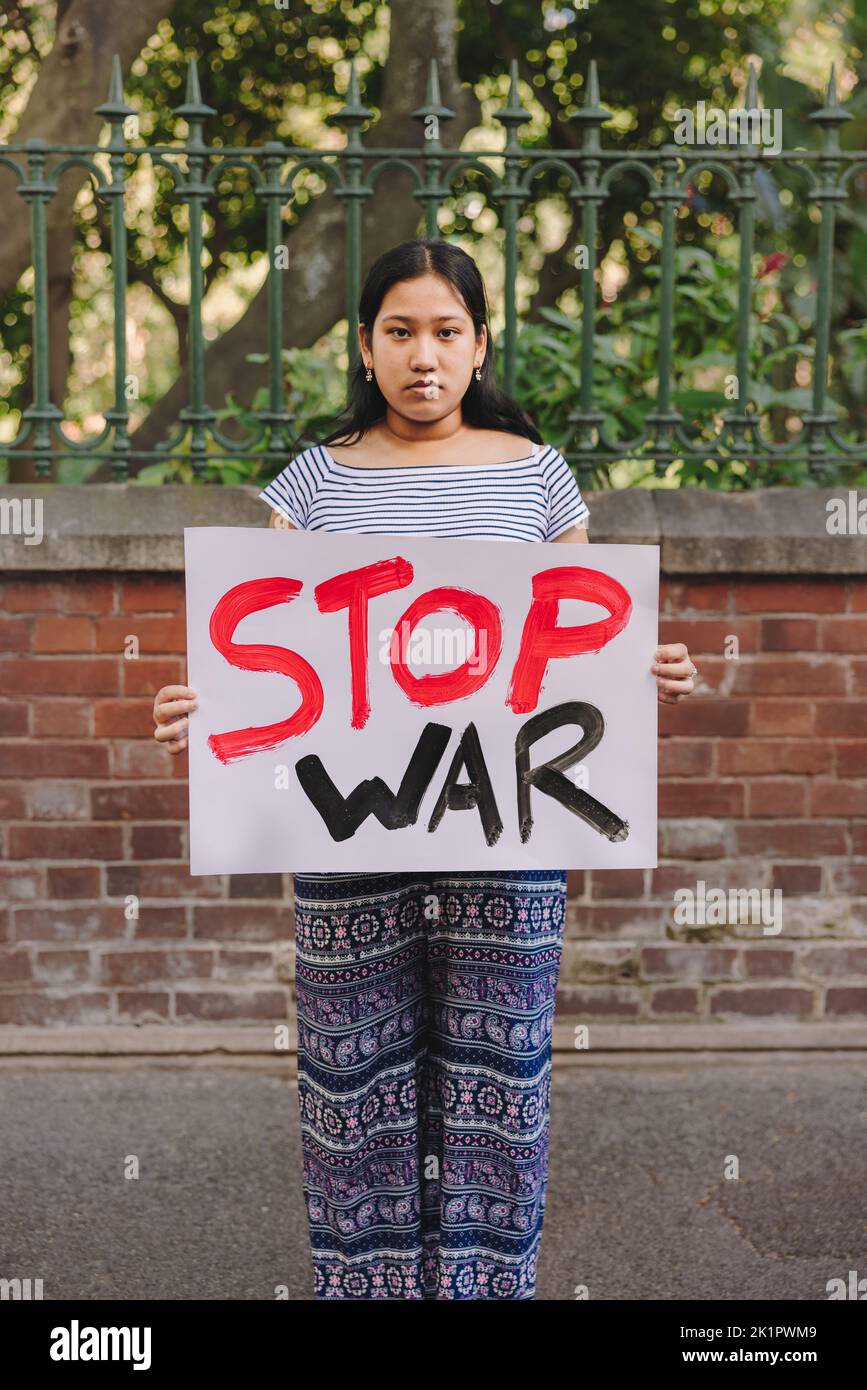 Adolescente ethnique regardant la caméra tout en tenant une affiche anti-guerre. Jeune militant de la paix protestant contre la guerre et la violence. Banque D'Images