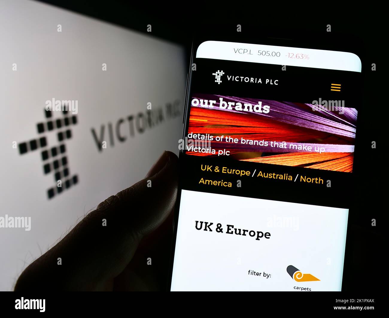 Personne tenant un téléphone portable avec la page Web de la société britannique de revêtement de sol Victoria plc à l'écran devant le logo. Concentrez-vous sur le centre de l'écran du téléphone. Banque D'Images