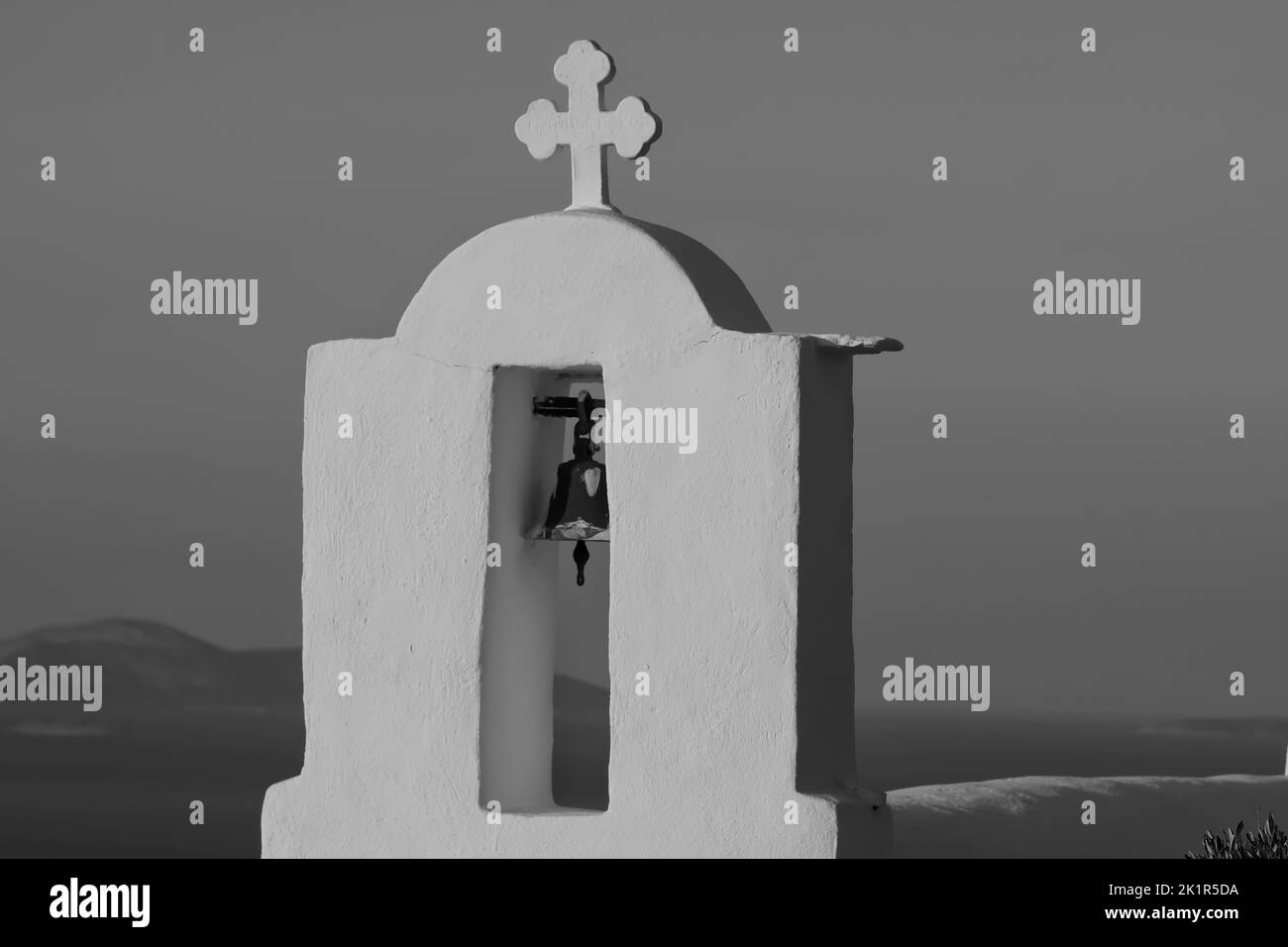 Une croix et une cloche sur le dessus d'une église orthodoxe dans iOS Grèce tandis que le soleil se couche dans le fond en noir et blanc Banque D'Images