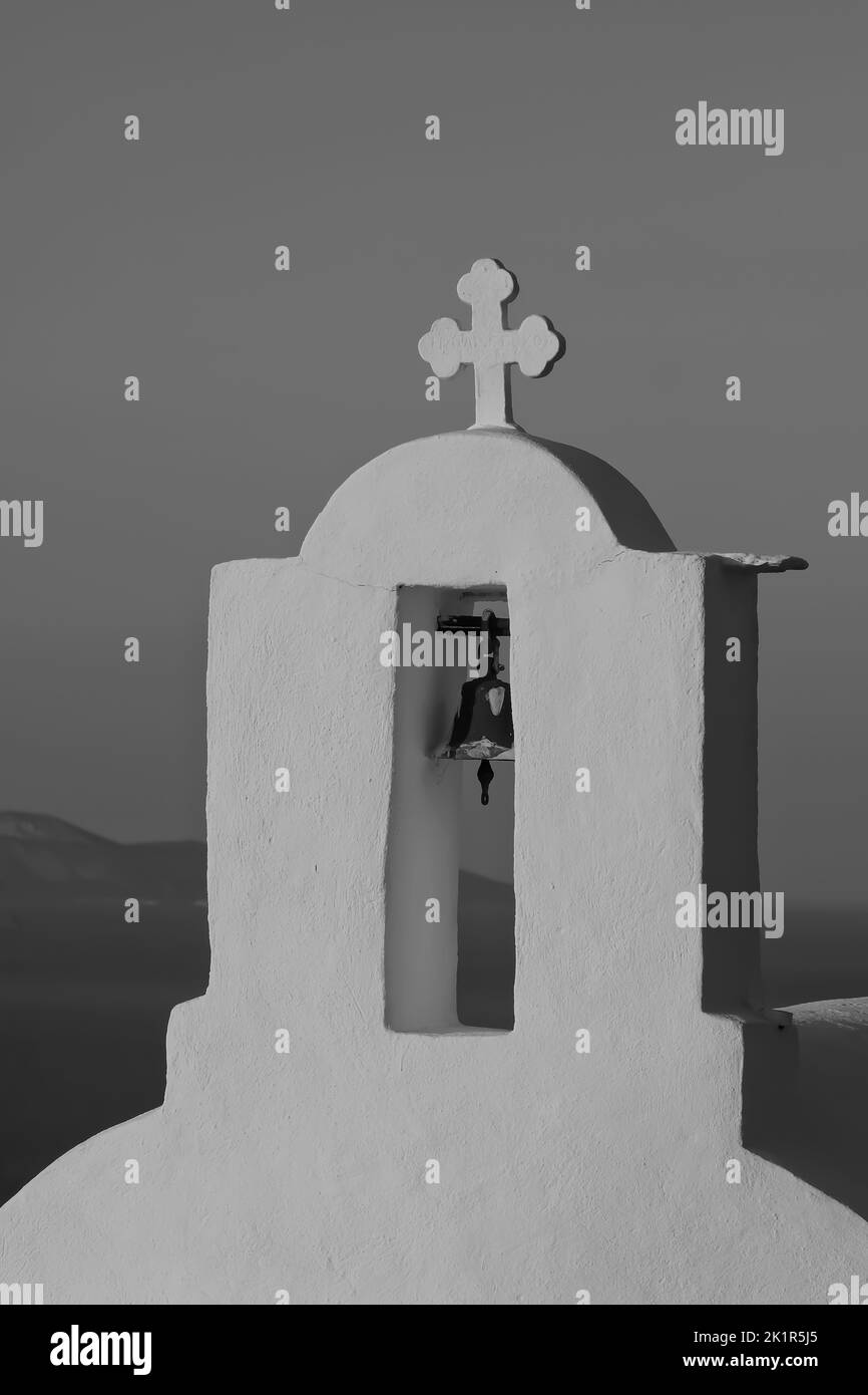 Une croix et une cloche sur le dessus d'une église orthodoxe dans iOS Grèce tandis que le soleil se couche dans le fond en noir et blanc Banque D'Images