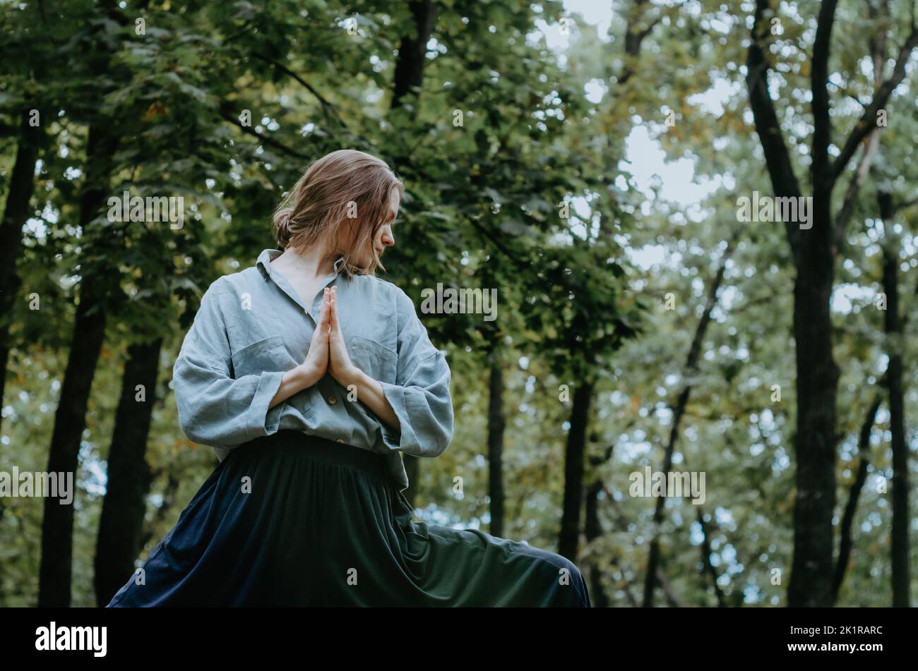 Vue latérale de la femme en posture de yoga du guerrier II avec les mains de prière namaste sur la poitrine, en regardant vers le bas Banque D'Images