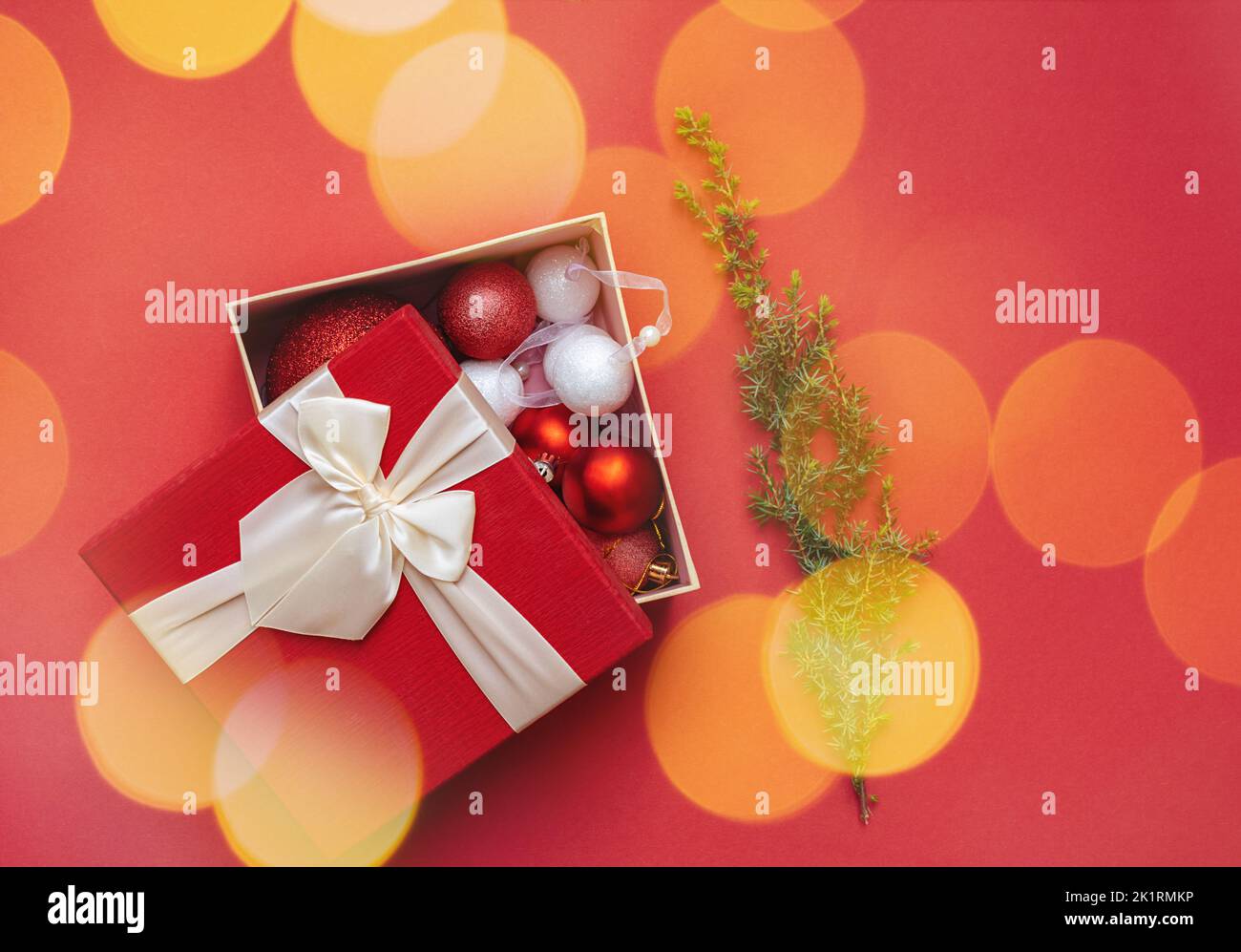 Décorations de Noël en boîte cadeau ouverte et bokhe doré aux perles rondes. Branche verte d'arbre de Noël sur fond rouge. Housse d'emballage avec noeud luxuriant. Joyeux Noël et Bonne Année. Copier l'espace. Banque D'Images