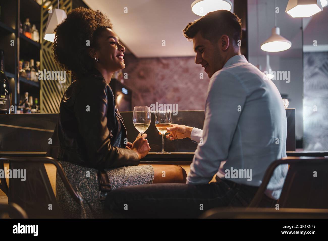 Couple romantique à une date parlant avec un verre de vin blanc assis au comptoir du bar dans la nuit - nourriture et boissons, personnes, concept de style de vie Banque D'Images
