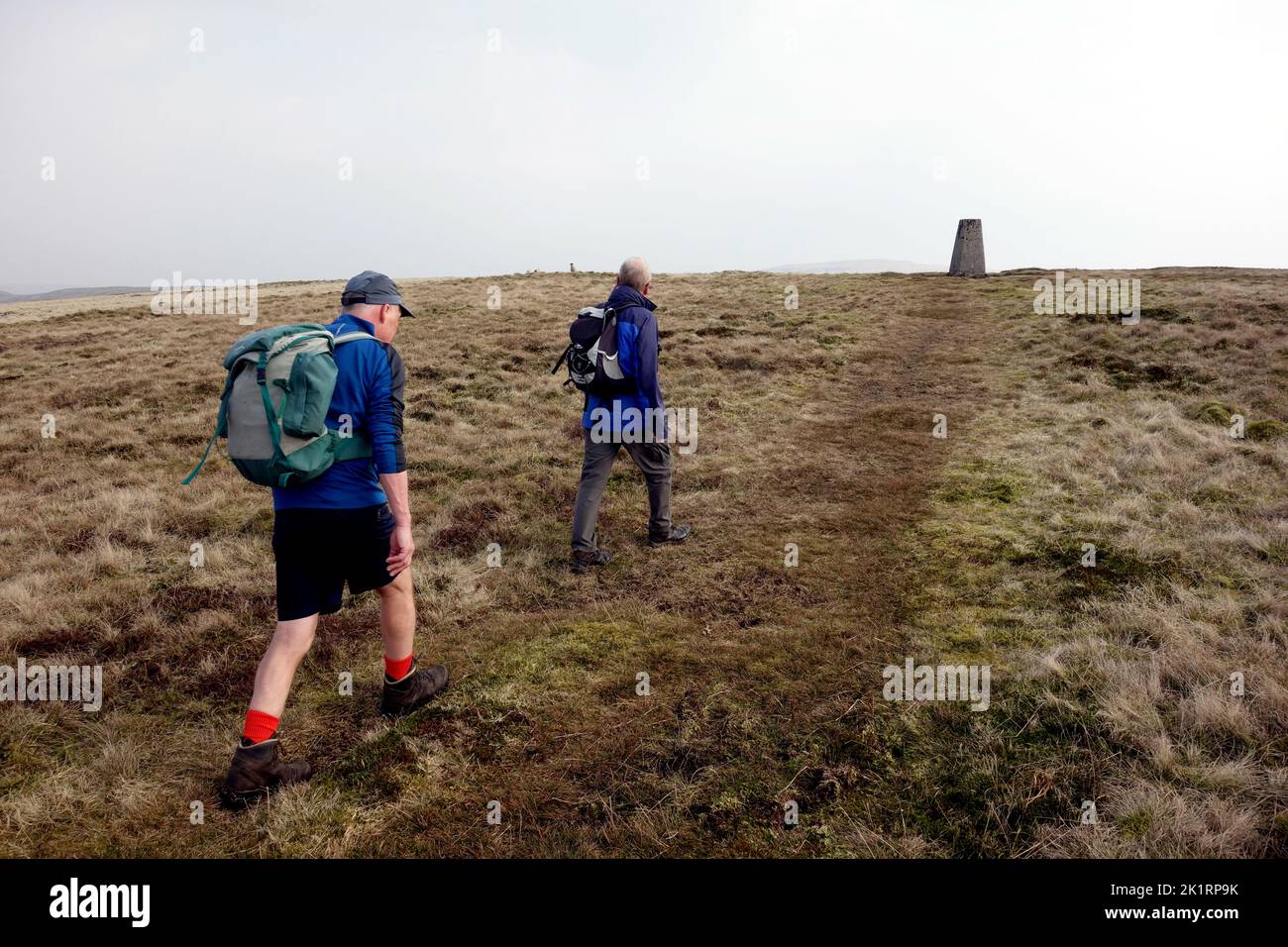 Deux hommes âgés marchant jusqu'au point de Trig Concrete sur le sommet de 'Gragareth' à Kingsdale dans le parc national de Yorkshire Dales, Angleterre, Royaume-Uni. Banque D'Images