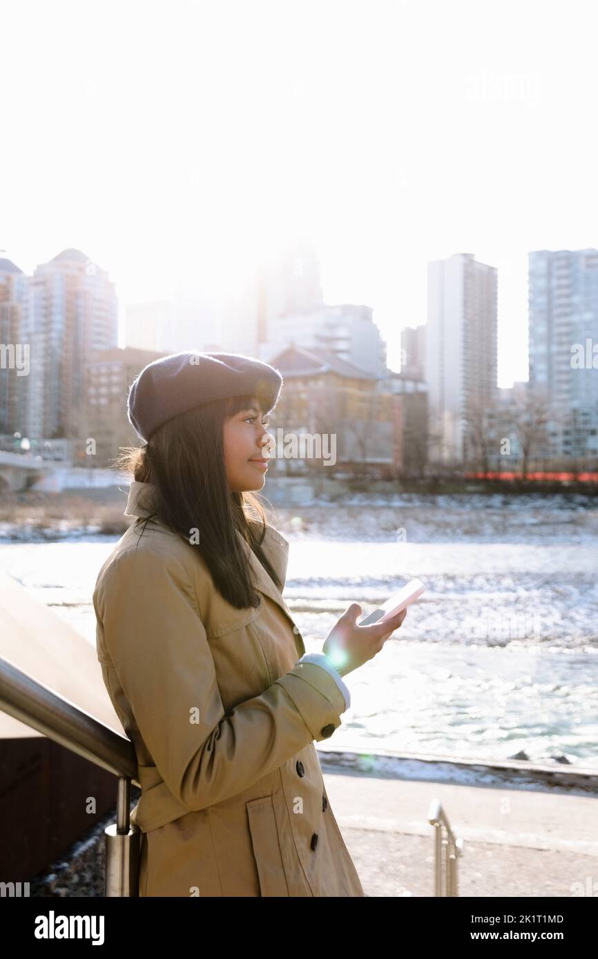 Jeune femme utilisant un smartphone le long du front de mer ensoleillé de la ville Banque D'Images