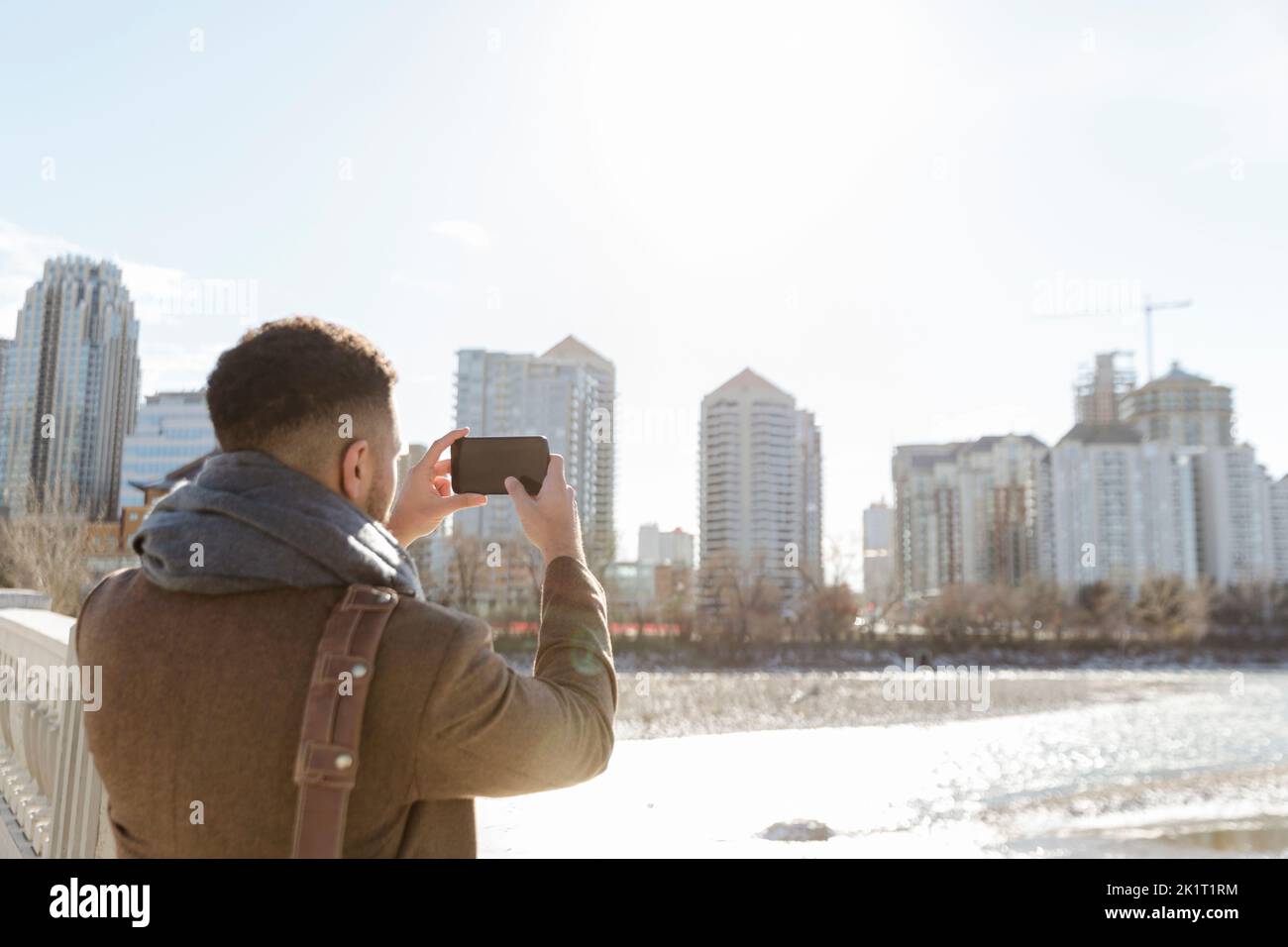 Touriste mâle utilisant un téléphone photo, photographier le paysage urbain ensoleillé depuis le pont Banque D'Images