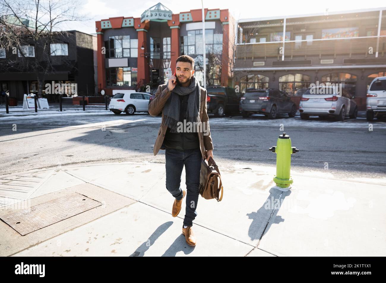 Jeune homme d'affaires avec porte-documents parlant sur un téléphone intelligent sur un trottoir urbain ensoleillé Banque D'Images