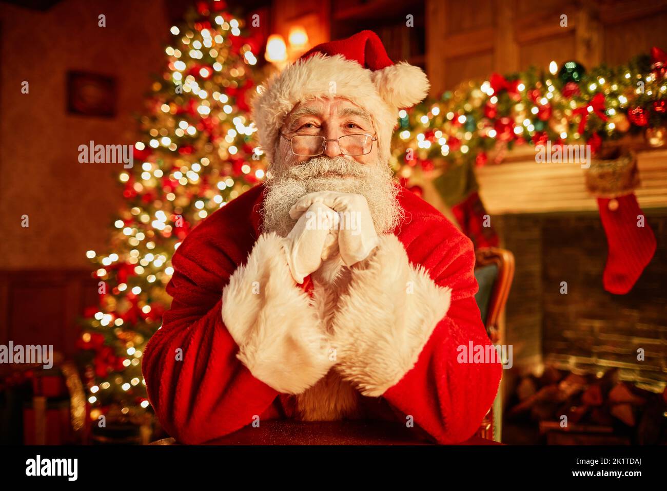 Vue de face portrait du Père Noël traditionnel souriant à l'appareil photo, tête reposant sur les bras avec l'arbre de noël en arrière-plan Banque D'Images