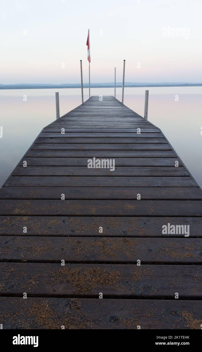 Un quai dans les premières teintes pastel de l'aube, minimalisme magique d'été sur un lac de calme parfait. Banque D'Images