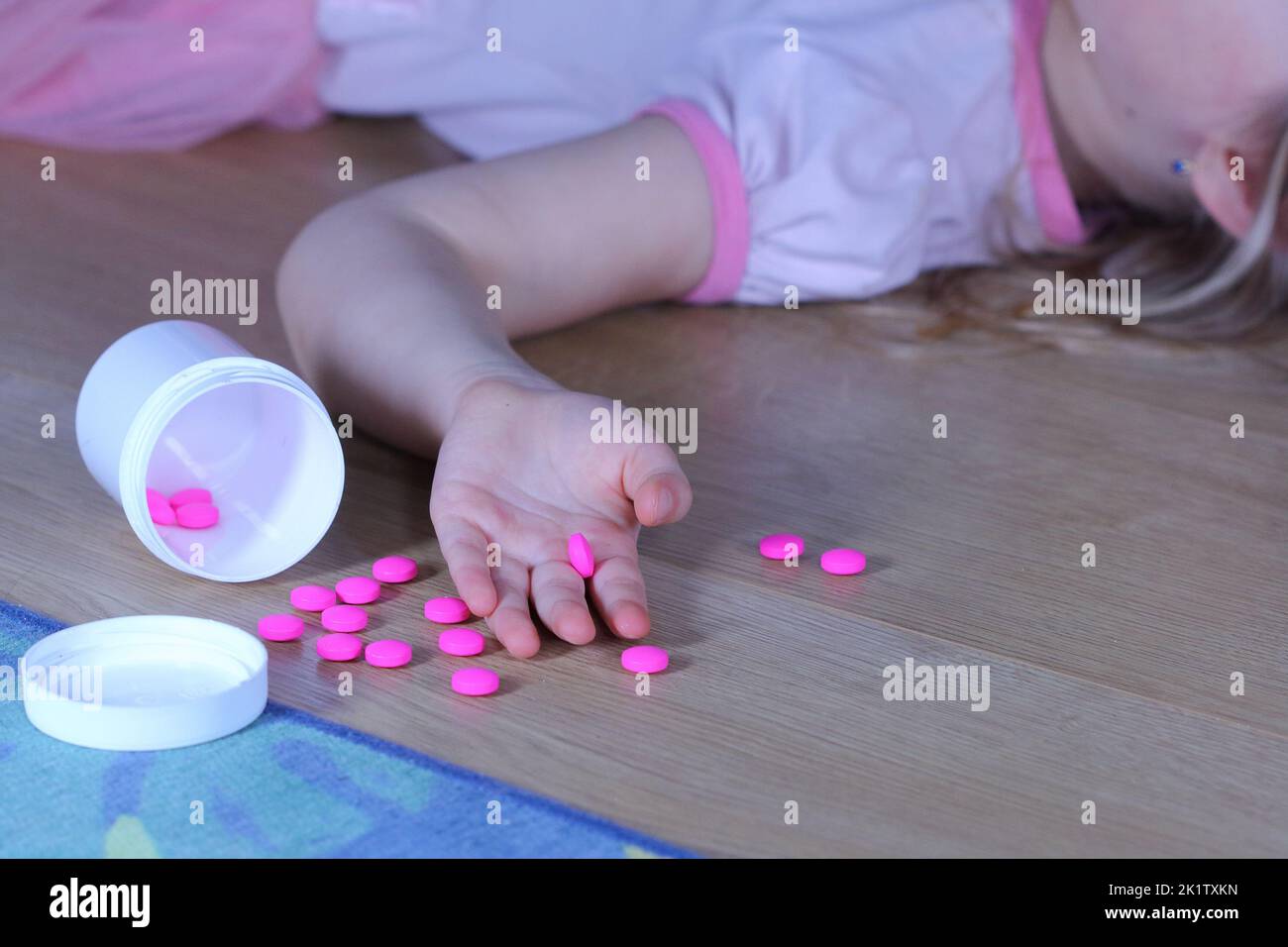 Petit enfant inconscient (fille) avec des pilules roses sur le sol à la maison. Danger d'intoxication médicamenteuse. Banque D'Images