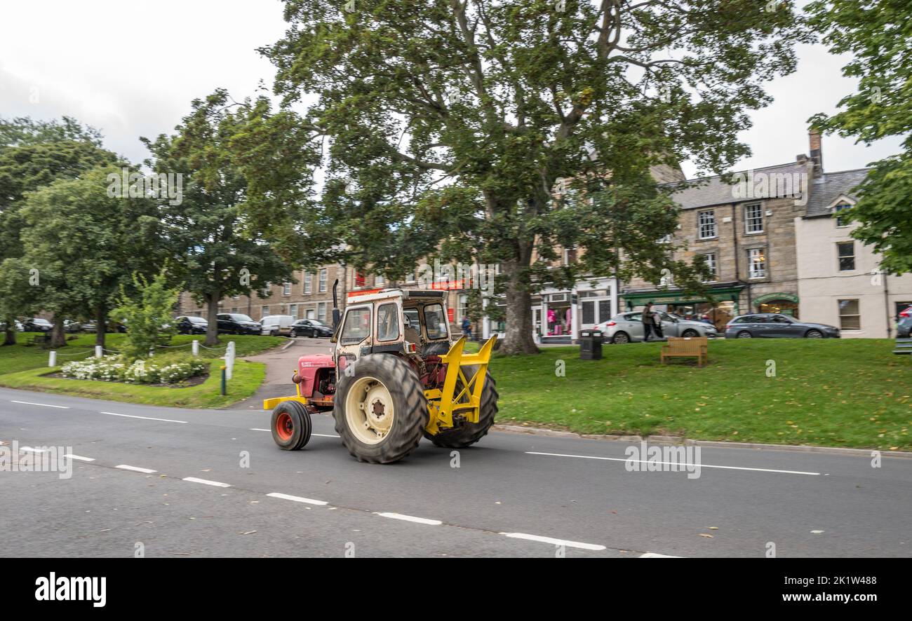 Tracteur d'époque descendant la route principale bordée d'arbres à travers la petite ville marchande de Rothbury, à Northumberland, en Angleterre. Banque D'Images