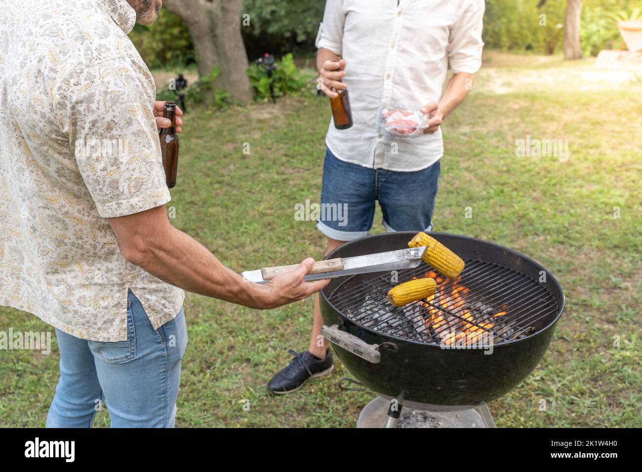 Les amis cuisent du maïs et de la viande avec le barbecue au feu et à la fumée. Banque D'Images