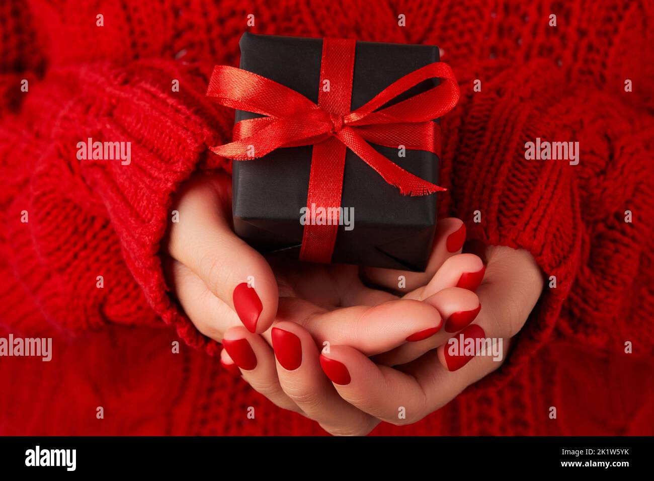 Mains de femmes manucures dans un chandail rouge contenant une boîte cadeau. Solde de Noël pour les Saint-Valentin Banque D'Images