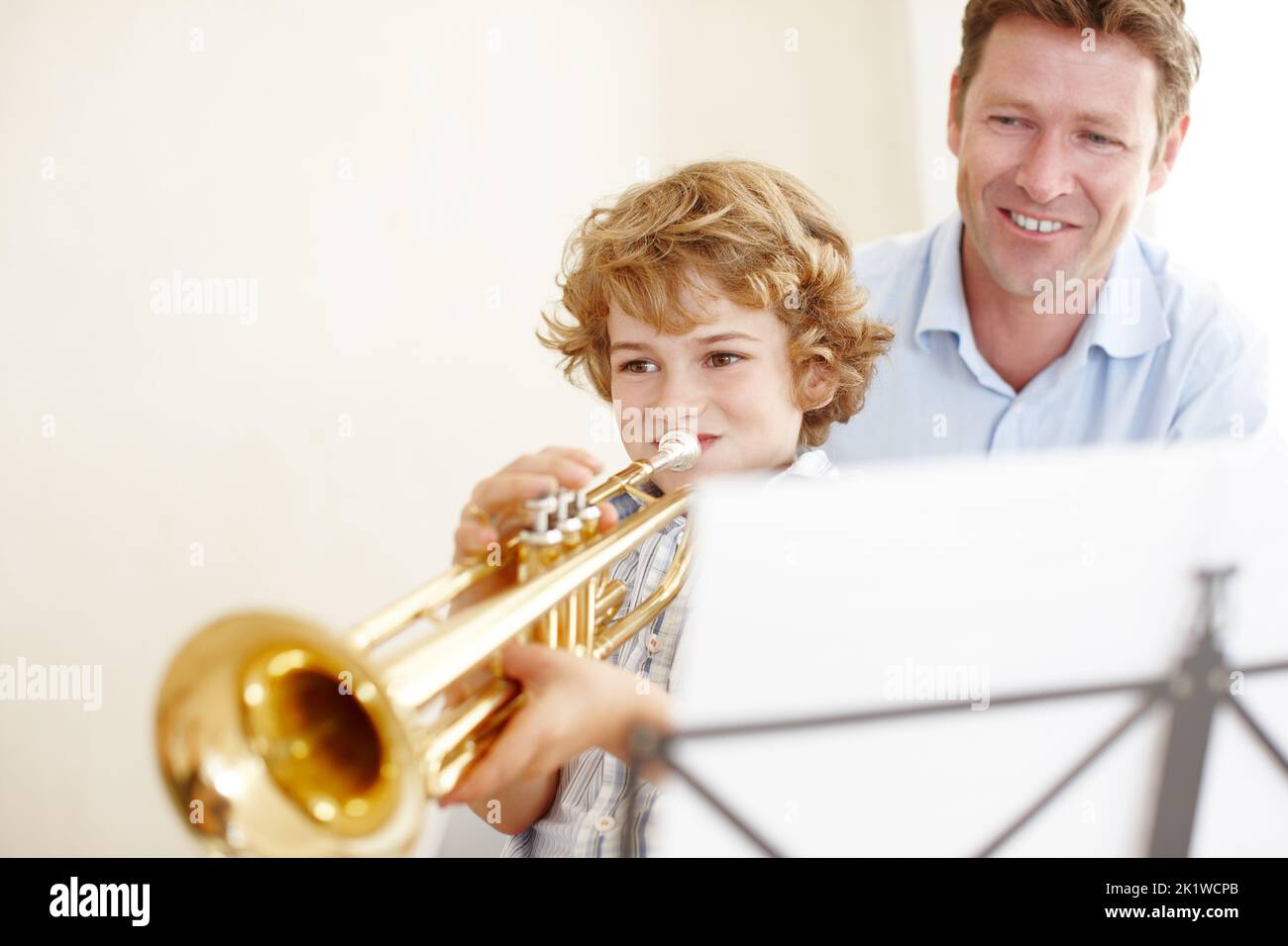 Un petit garçon mignon jouant la trompette tandis que son père le regarde fièrement. Banque D'Images