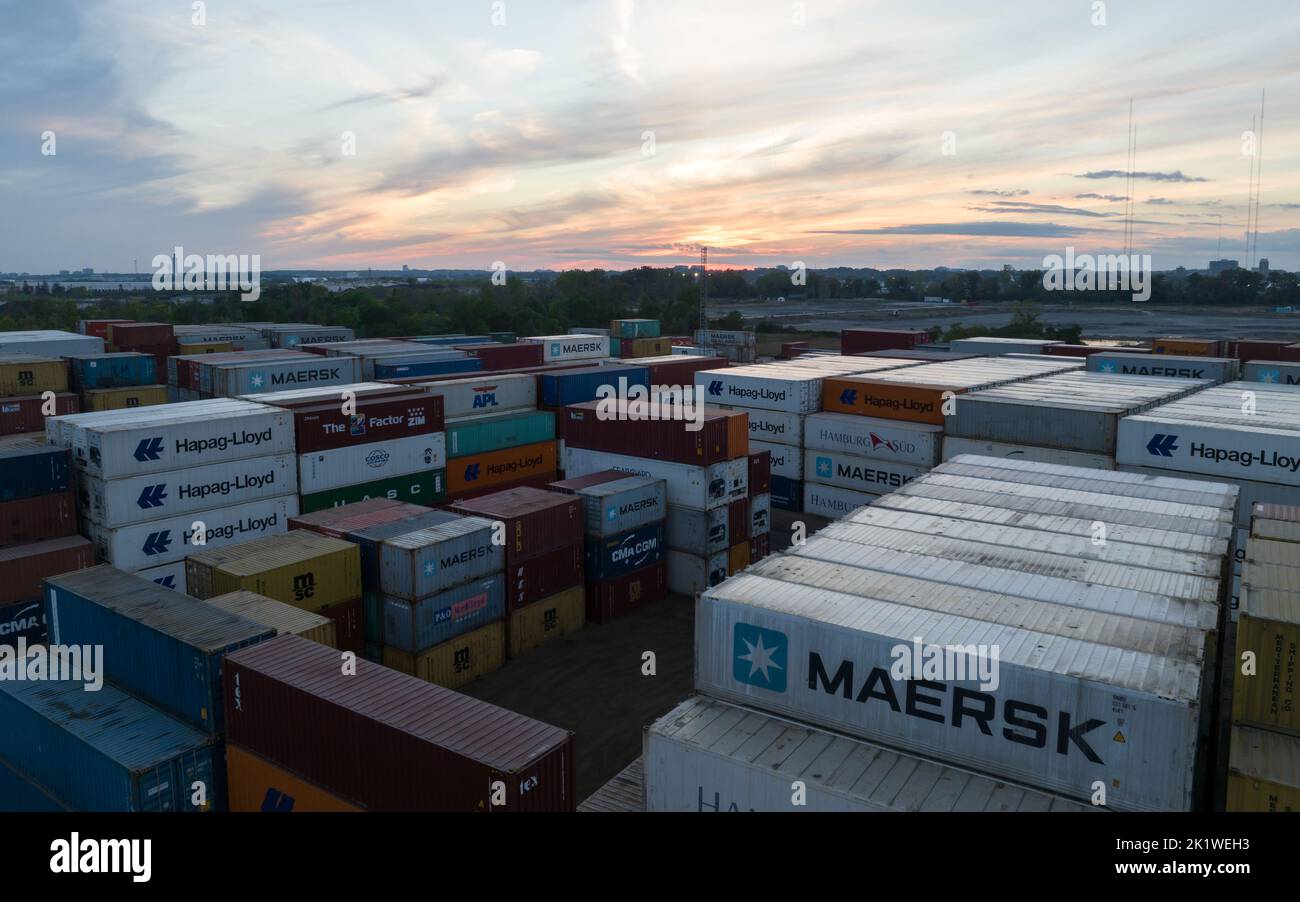 Une vue aérienne au-dessus d'un terminal de navigation dans un vaste secteur industriel vu au crépuscule ; les grands transporteurs internationaux de transport maritime ont des conteneurs empilés dans le stockage. Banque D'Images