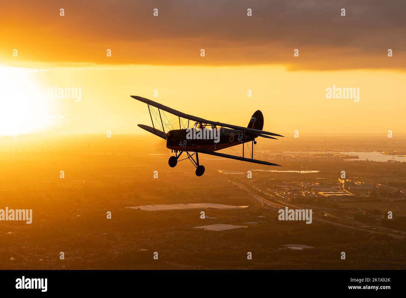 Un entraîneur de Stampe-Vertongen SV.4 en biplan survolant Anvers pendant un beau coucher de soleil. Banque D'Images