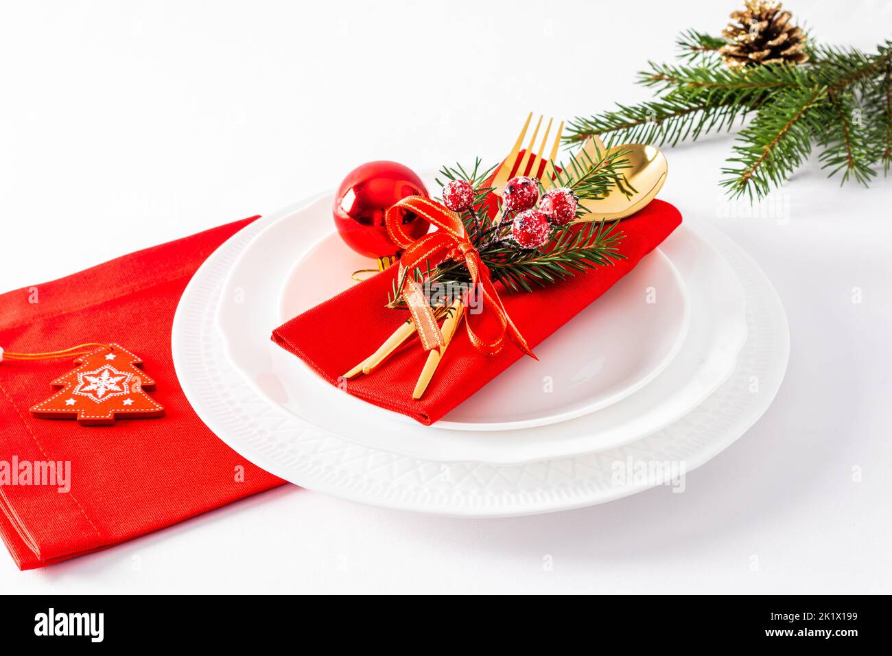 Assiettes blanches avec serviettes rouges et décorations de Noël sur fond blanc. Service festif dans le style classique Banque D'Images