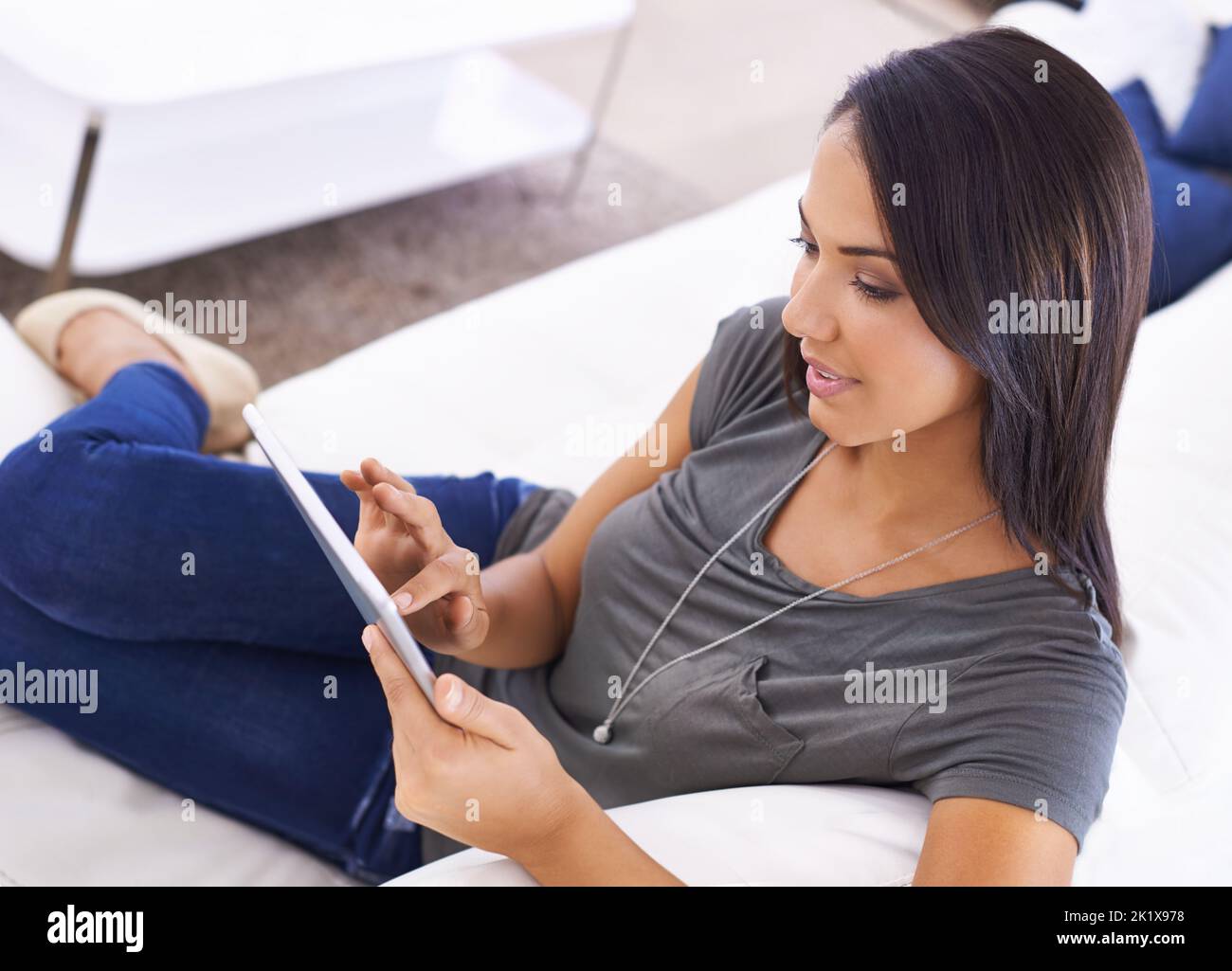La communication a rendu la conventice. Une jeune femme attrayante utilisant sa tablette numérique à la maison Banque D'Images