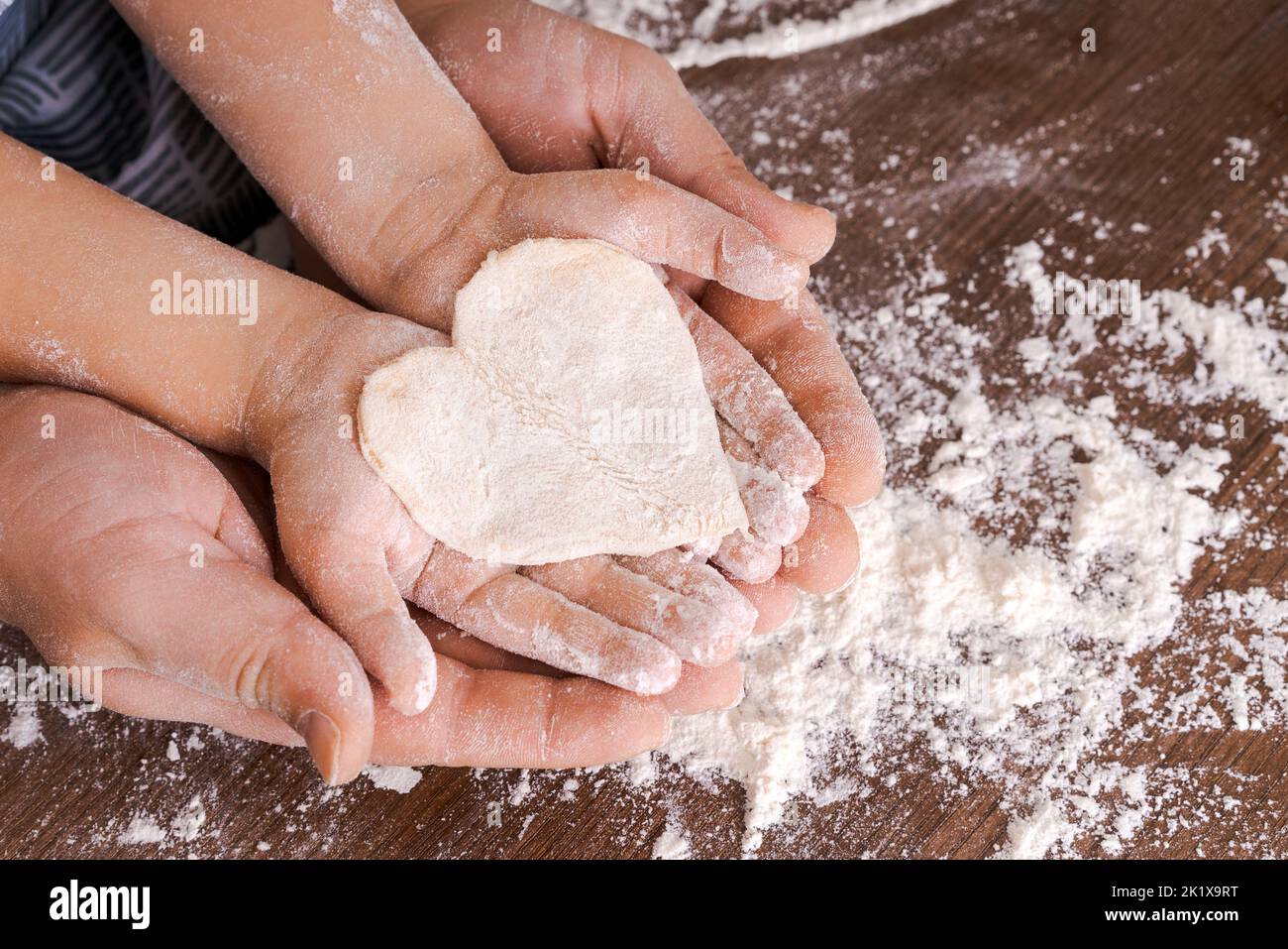 Vue de dessus la main du père et de l'enfant, découpez des biscuits en forme de coeur de la pâte sur les mains sur le fond d'une table en bois avec de la farine en vrac. Défaillance de l'écran plat. Banque D'Images