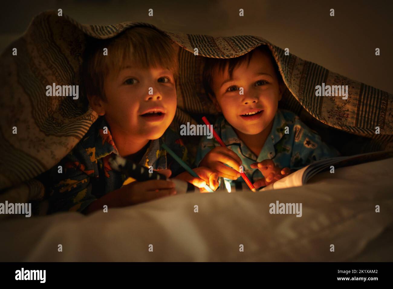 Maman dit que la lumière garde les mauvaises choses loin. Portrait de deux frères allongé sous leur couverture colorante en images avec une lampe de poche Banque D'Images