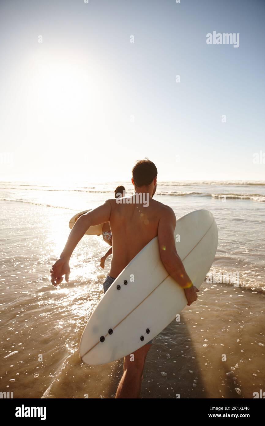 Laisse le surf. Photo d'un jeune couple de surfeurs qui s'infilent ensemble dans la mer. Banque D'Images