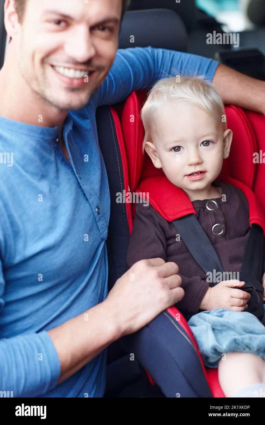S'occuper de mon fils. Portrait d'un père souriant à côté de son tout-petit qui est assis dans son siège de bébé. Banque D'Images