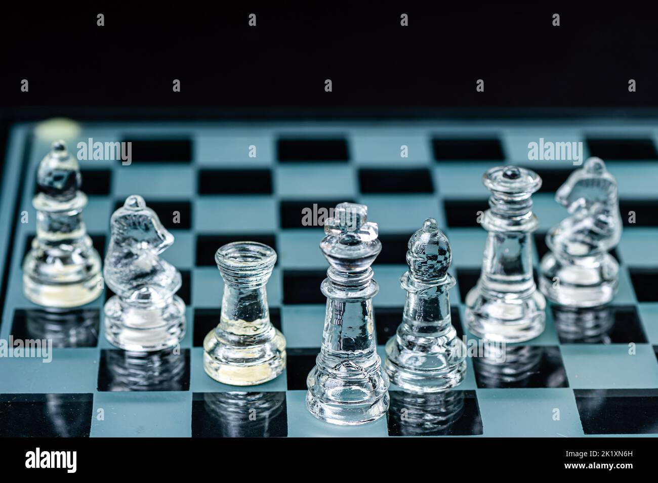 personnages d'échecs en verre transparent disposés en rangée et reflétant dans un échiquier en verre. Isolé sur le noir Banque D'Images