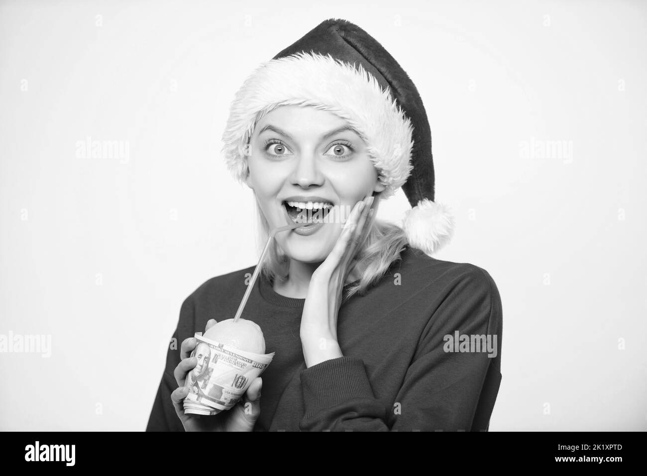 Symbole de richesse et de richesse. Fille avec citron et argent. Concept d'argent citron. Chapeau de père noël fille boit jus de citron emballé dans un billet de banque. Totalement naturel Banque D'Images