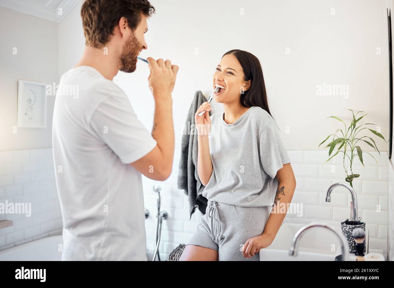 L'amour, le matin et le couple dans la salle de bains se brossant les dents ensemble faisant la routine quotidienne, heureux et sourire. Homme et femme ayant une bonne santé dentaire, soins de la bouche a Banque D'Images