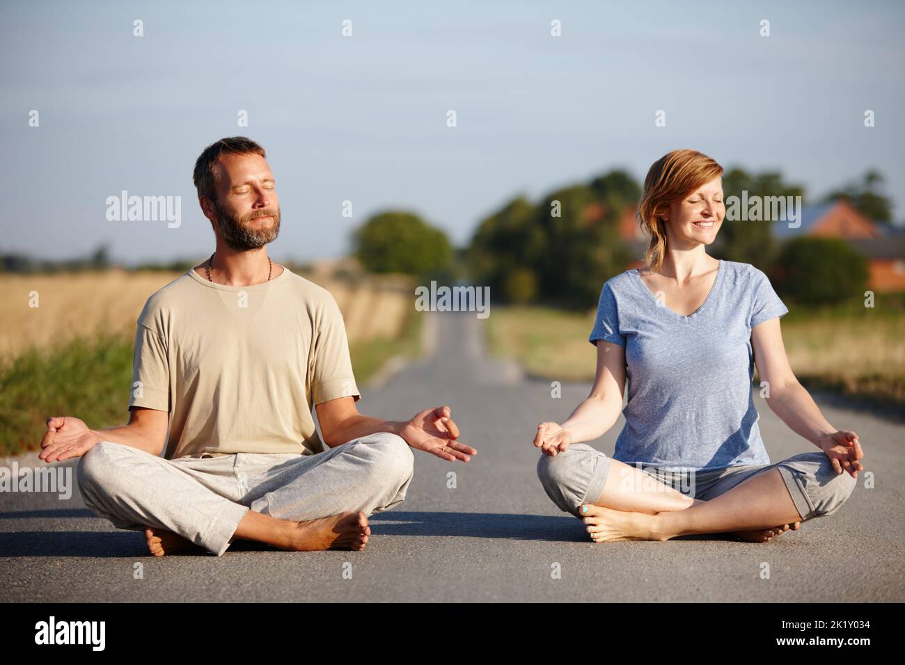 Trouver la paix intérieure ensemble. Un couple serein assis dans la position de lotus sur une route de campagne. Banque D'Images