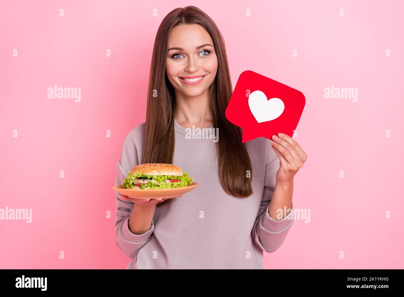 Photo de fille attrayante main tenir cheeseburger papier comme carte isolée sur fond rose couleur Banque D'Images