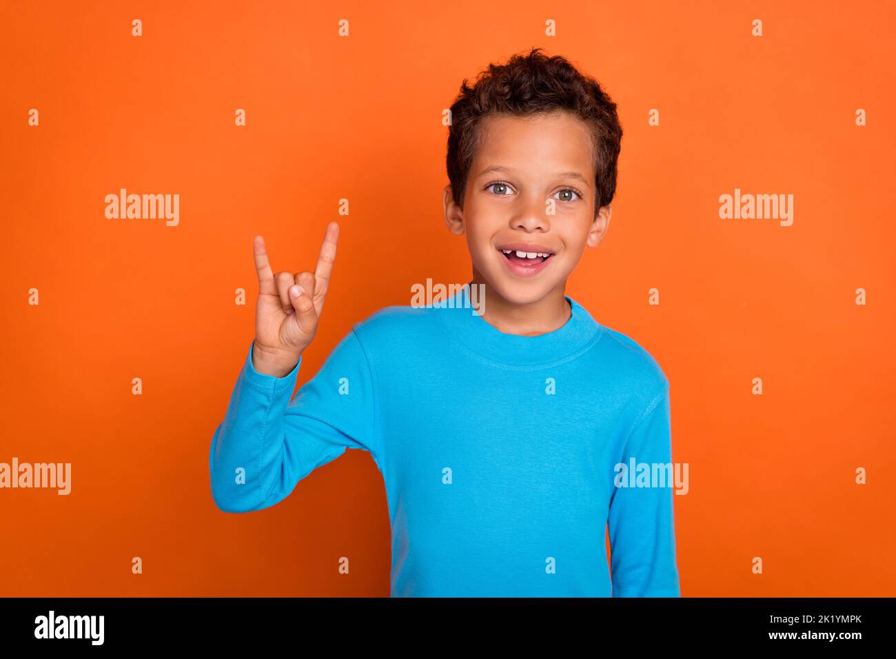 Photo de gai garçon amateur de musique montrer le bras démontrer la liberté de rock symbole habillé bleu branché pull isolé sur fond de couleur orange Banque D'Images