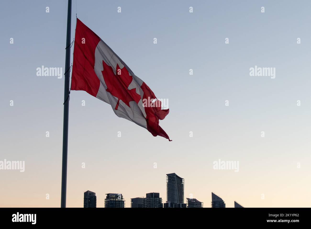 Un grand drapeau canadien est vu tôt le matin par temps clair, près d'un horizon moderne. Banque D'Images