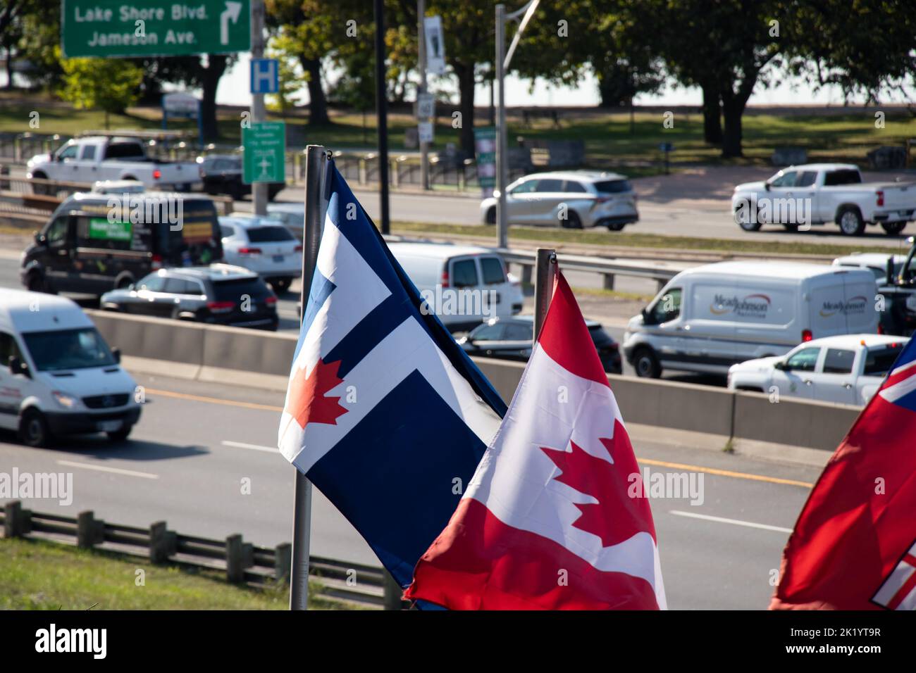 Le drapeau de la ville de Toronto et le drapeau canadien sont vus agitant par une journée ensoleillée le long d'une route très fréquentée Gardiner Expressway, au centre-ville de Toronto. Banque D'Images