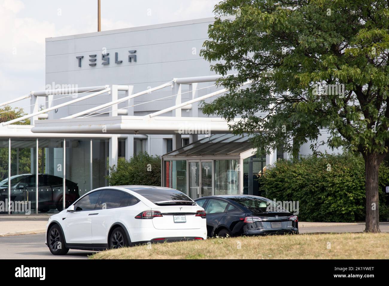 L'avant d'un concessionnaire Tesla est vu pendant la journée avec un modèle X blanc et un modèle 3 noir à l'avant, tandis qu'un véhicule de démonstration peut être vu dans le bâtiment. Banque D'Images