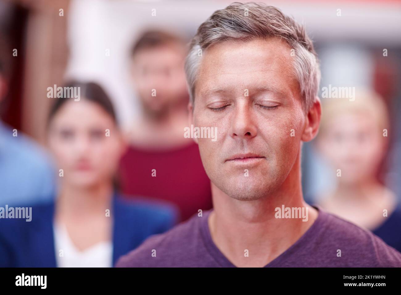 Restez calme et continuez. Un employé de bureau debout avec ses yeux fermés avec ses collègues en arrière-plan Banque D'Images