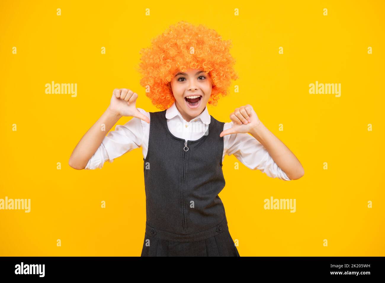 Anniversaire fête d'enfants. Drôle d'enfant dans la perruque clown curly isolé sur fond jaune. Visage excité, émotions gaies de la jeune fille. Banque D'Images