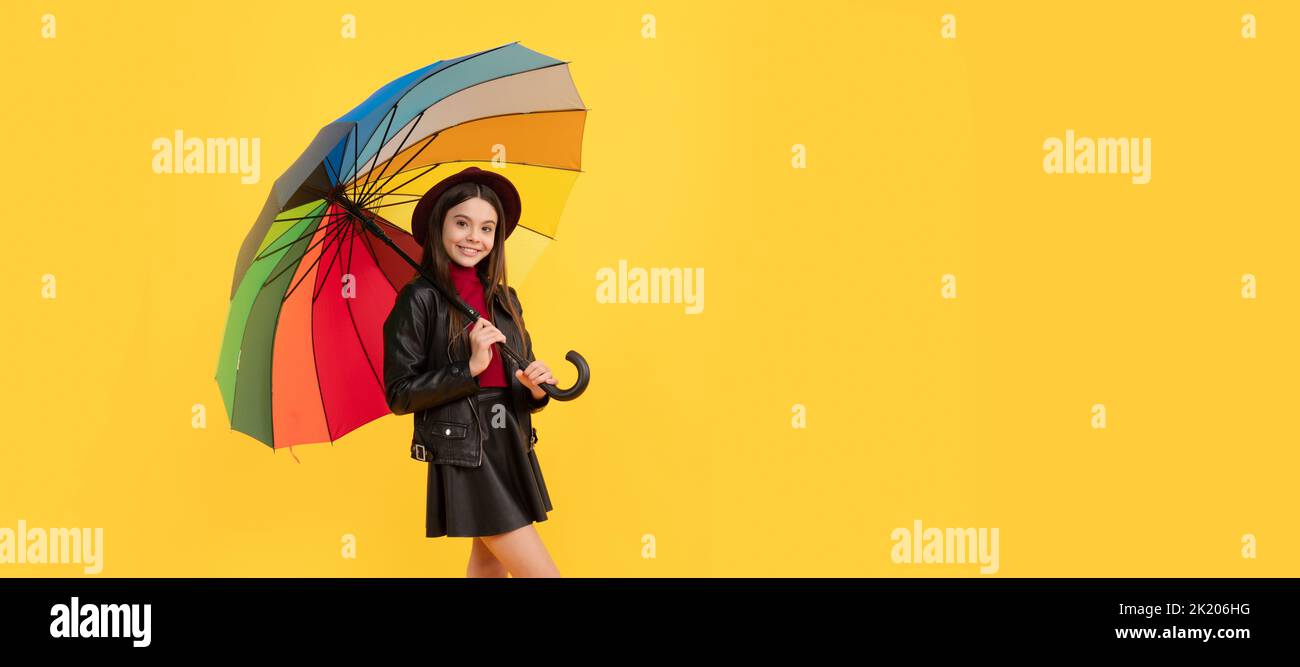 bonne jeune fille en chapeau et vêtements en cuir sous parapluie arc-en-ciel, temps d'automne. Enfant avec parapluie d'automne, temps pluvieux, affiche horizontale Banque D'Images