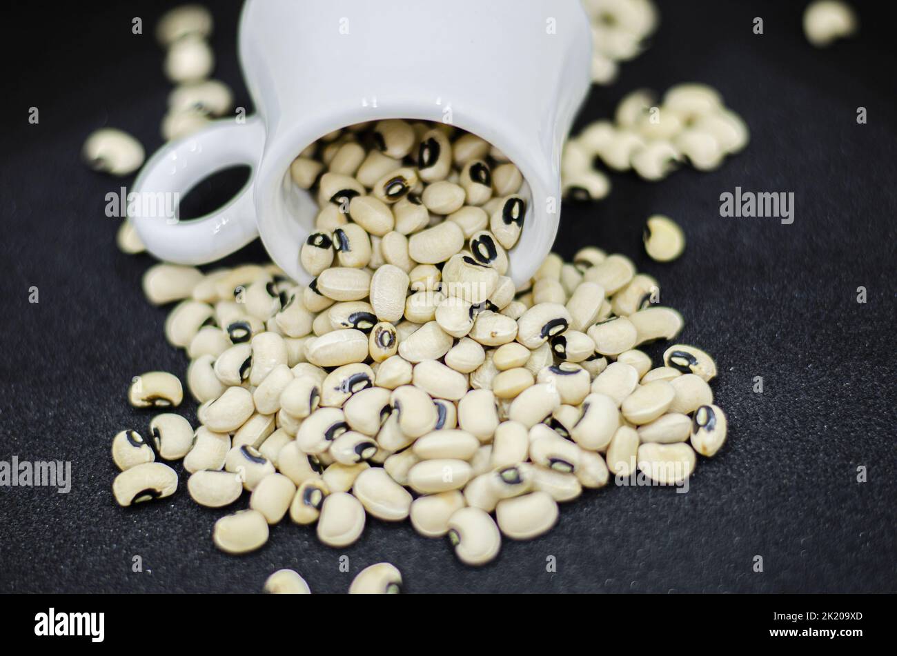 Haricots à yeux noirs déversant d'une tasse sur fond noir, haricots secs sur fond noir Banque D'Images