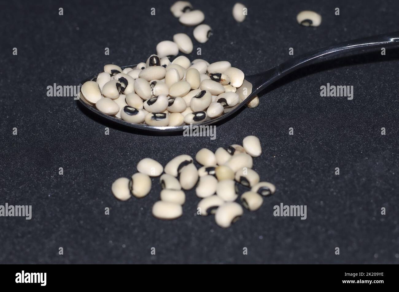 Haricots secs à yeux noirs dans une cuillère à soupe renversée sur fond noir. Mise au point sélective, haricots secs sur fond noir Banque D'Images