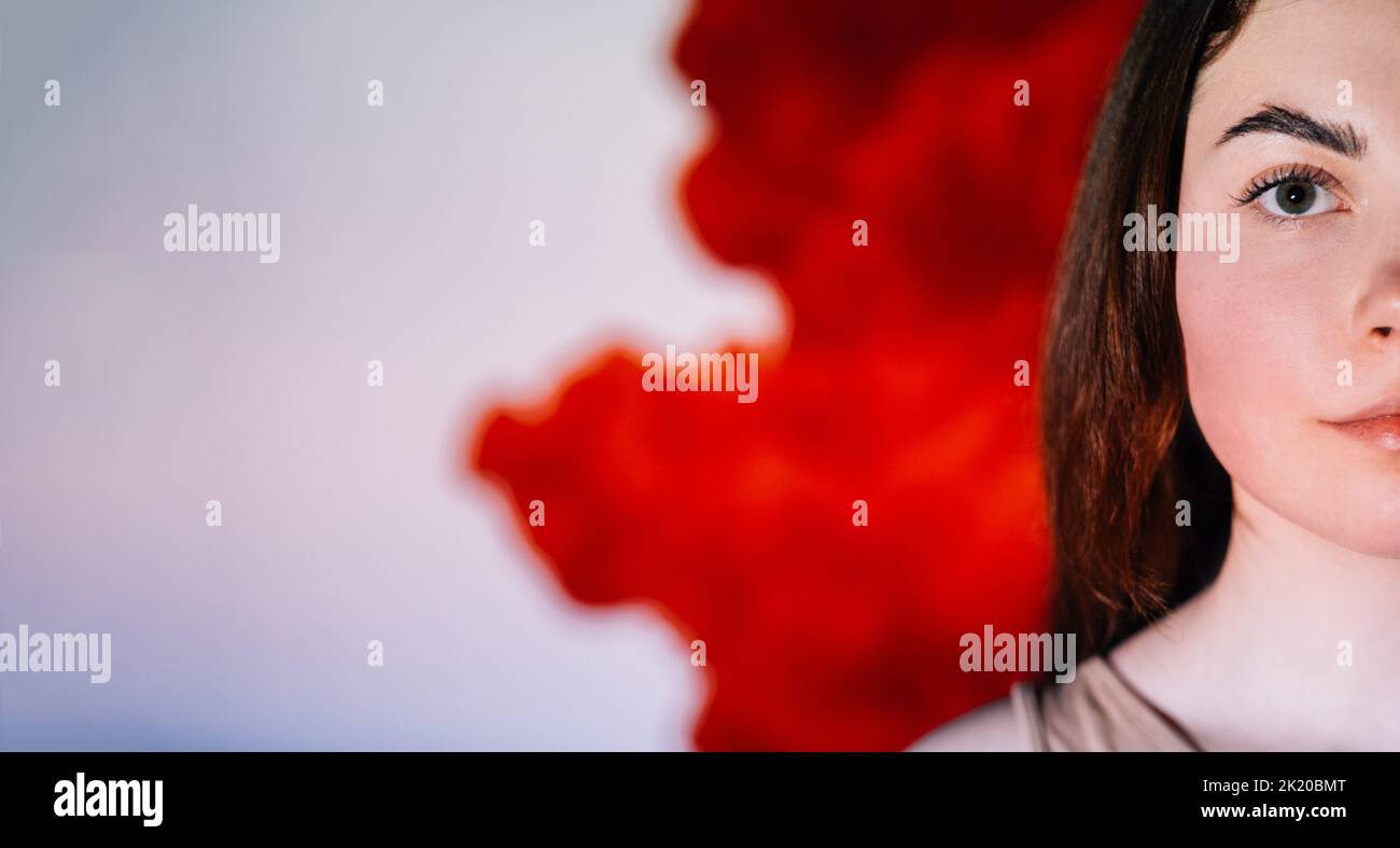 Sensibilisation au SIDA. Cancer du sang. Mois du VIH. Santé des personnes. Portrait demi-visage de femme sérieuse isolée sur un flux de couleur rouge vif défoqué sur W Banque D'Images