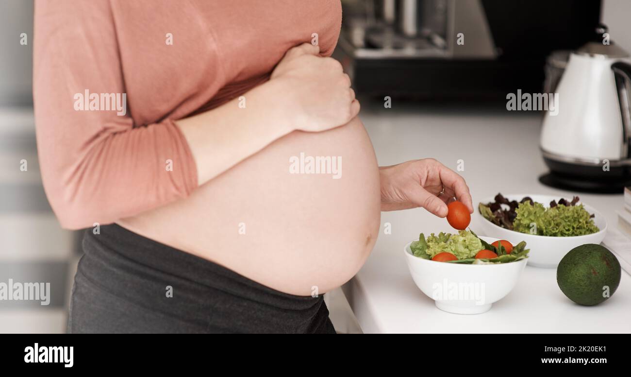 Manger pour deux. Une jeune femme enceinte qui mange une salade dans la cuisine. Banque D'Images