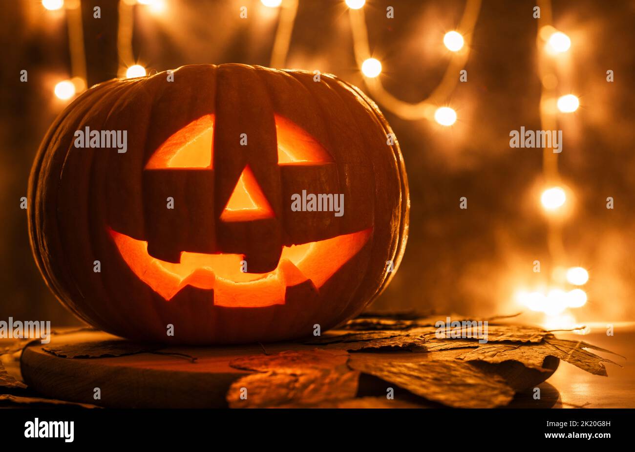 Lanterne Jack à tête de citrouille d'Halloween sur fond sombre avec feuilles sèches. Les visages brillants se gâteries ou se gâteries Banque D'Images